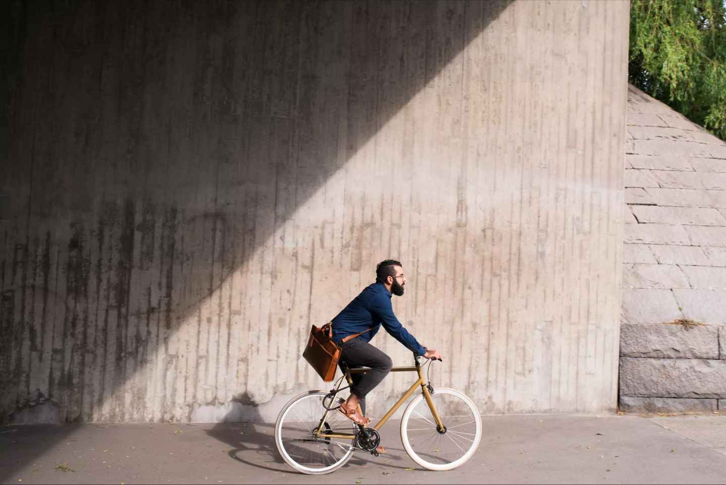 Person med arbetsväska cyklar genom staden i solskenet.