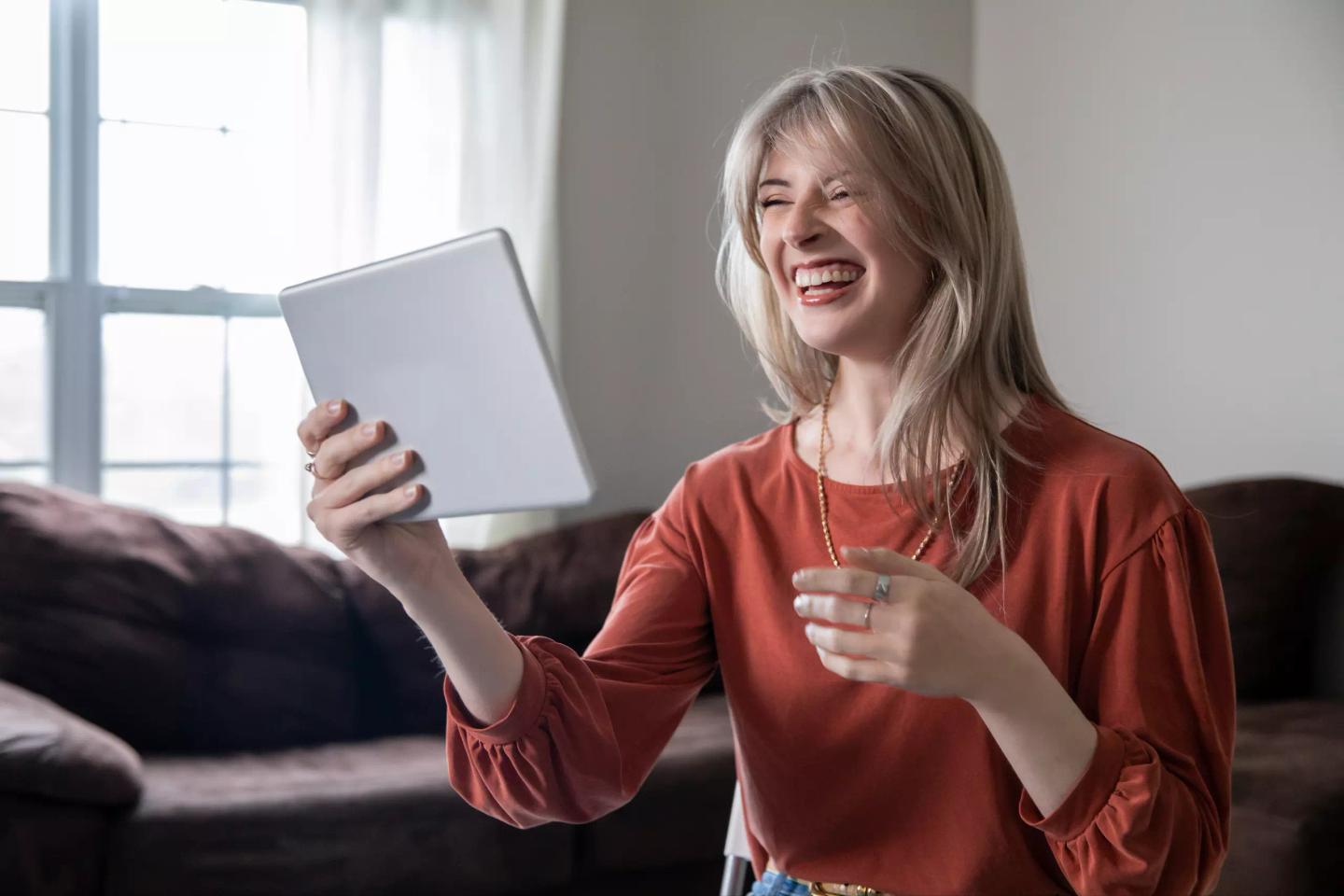 Skrattande kvinna deltar i digitalt möte på iPad från vardagsrummet.