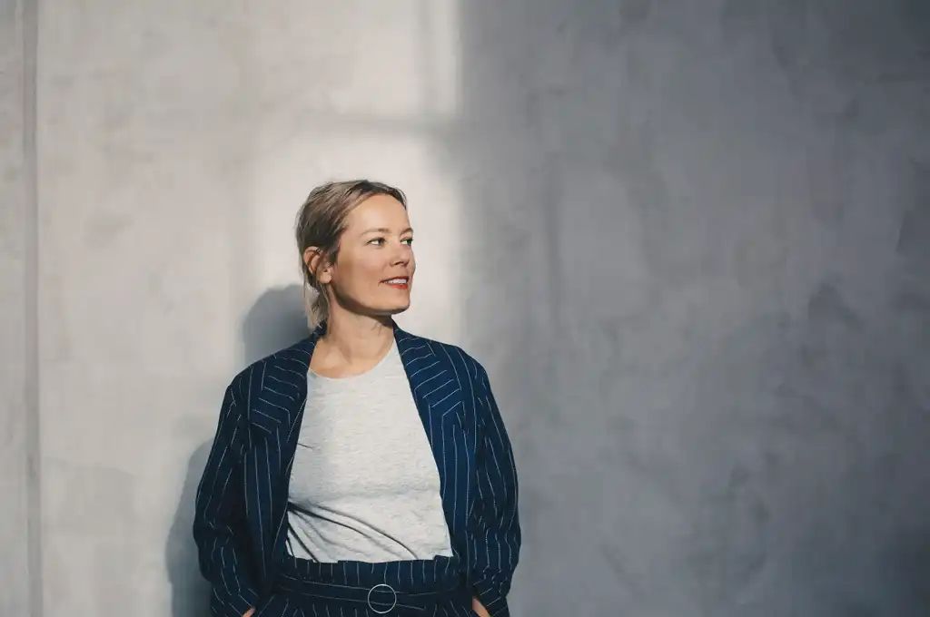 Ung affärsklädd person med händerna i fickorna och ett leende på läpparna.