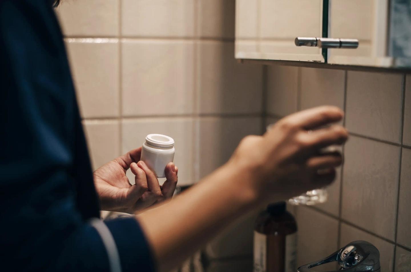 Närbild av händerna på en person som tar piller från badrumsskåpet.