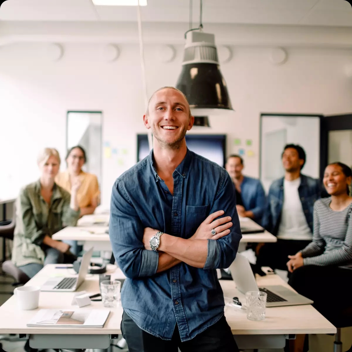 En nöjd chef ler mot kameran i kontorsmiljö med hela sitt team bakom sig.