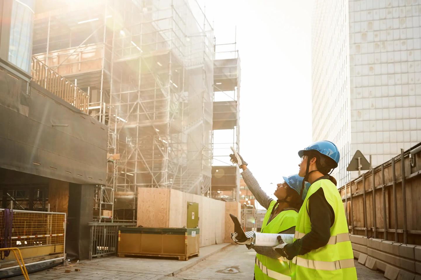 Två personer med hjälmar och reflexvästar inspekterar en ny byggnad under uppförande.