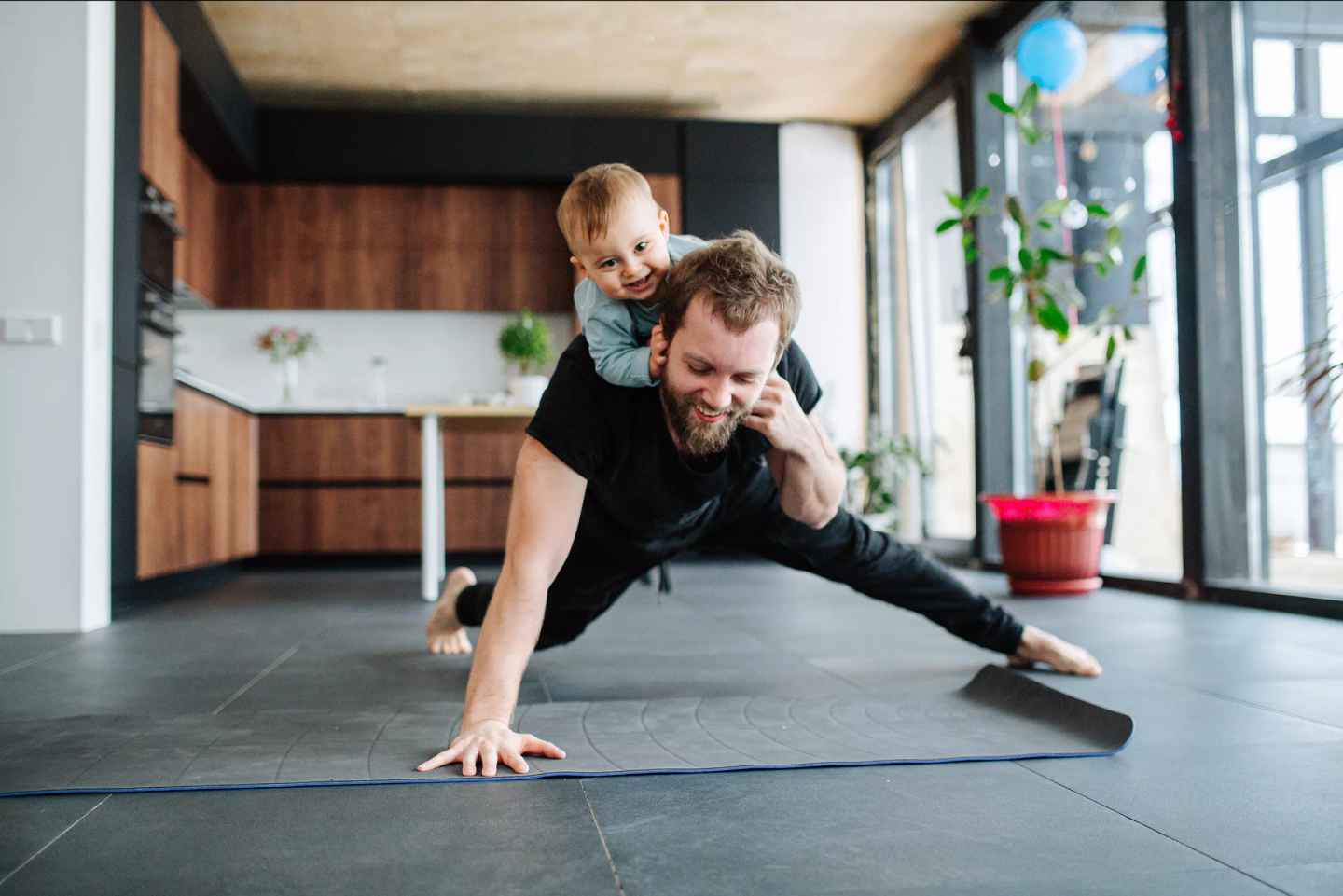 Förälder tränar på golvet hemma med ett litet barn på ryggen.